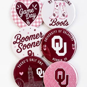 May include: Six circular pin-back buttons featuring University of Oklahoma themes. Designs include a gingham heart with 'Game Day', pink cowboy boots with 'My Tailgating Boots', 'Boomer Sooner' text, the OU logo, a campus building, and 'Sooner Girl'.
