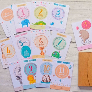 May include: A set of 11 baby milestone cards with colorful illustrations of animals and the text "Oggi Compio" (meaning "Today I Turn") in Italian. The cards are numbered 1 through 11, representing each month of the baby's first year.