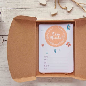 May include: A light brown box with a white card inside. The card has a peach-colored circle with the text "Ciao Mondo!" in a white circle with green leaves. The card also has butterflies and a section for writing information.