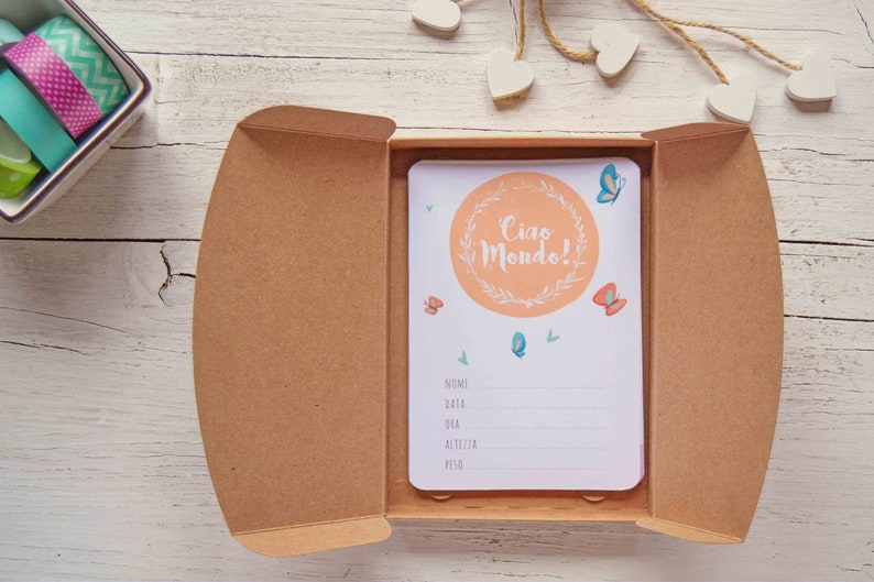 May include: A light brown box with a white card inside. The card has a peach-colored circle with the text "Ciao Mondo!" in a white circle with green leaves. The card also has butterflies and a section for writing information.