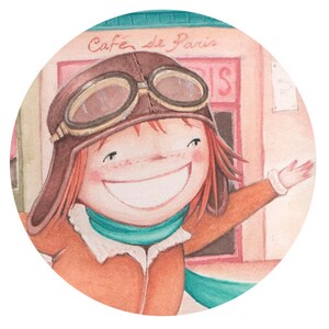 Puede incluir: Una ni&ntilde;a sonriente que lleva un gorro de aviador de cuero marr&oacute;n con gafas, una chaqueta marr&oacute;n y una bufanda turquesa. Est&aacute; de pie frente a un edificio con un cartel que dice "Cafe de Paris".