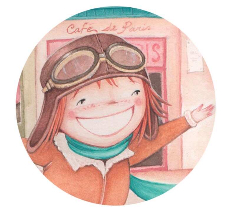 Puede incluir: Una ni&ntilde;a sonriente que lleva un gorro de aviador de cuero marr&oacute;n con gafas, una chaqueta marr&oacute;n y una bufanda turquesa. Est&aacute; de pie frente a un edificio con un cartel que dice "Cafe de Paris".