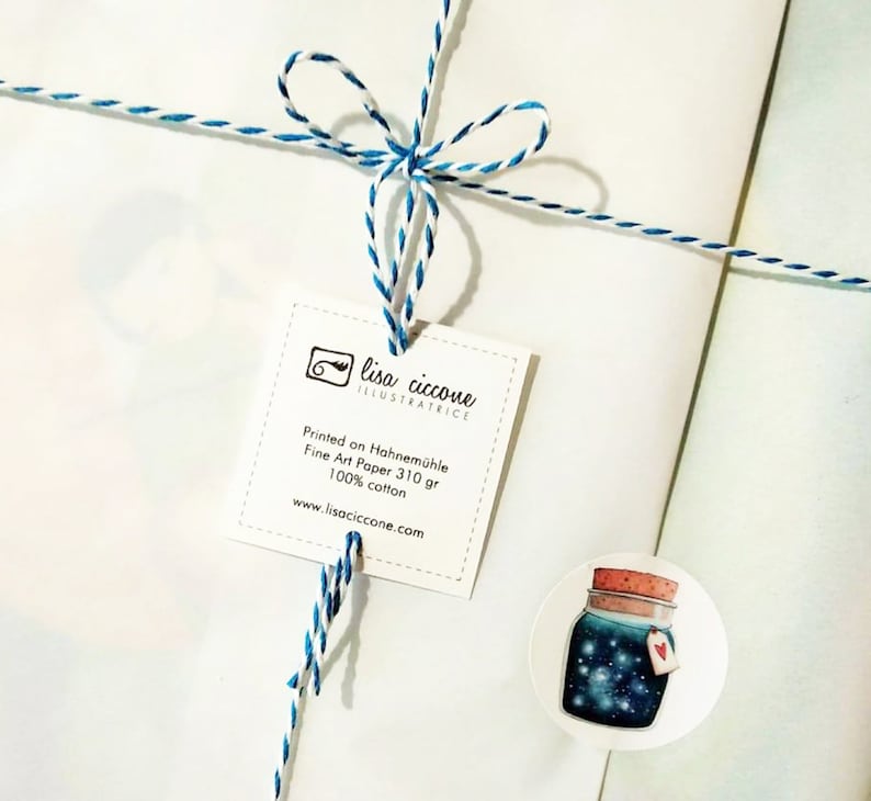 Puede incluir: Un sobre blanco con un lazo de cuerda azul y blanco. Una etiqueta blanca con el texto "lisa ciccone ILLUSTRATRICE" est&aacute; unida a la cuerda. La etiqueta tambi&eacute;n incluye el texto "Printed on Hahnem&uuml;hle Fine Art Paper 310 gr 100% cotton www.lisaciccone.com". Una pegatina redonda con una ilustraci&oacute;n de acuarela de un frasco lleno de estrellas est&aacute; pegada al sobre.