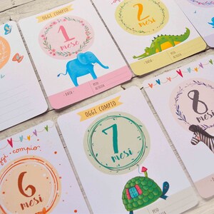 May include: A set of ten baby milestone cards with colorful illustrations of animals and the text "Oggi compio" (meaning "Today I turn") and the number of months. The cards are designed for a baby's first year.