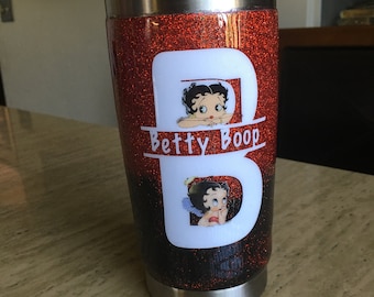 Op de afbeelding: Een roestvrijstalen tumbler met een rode en zwarte glitterafwerking. De tumbler heeft een witte afbeelding van het personage Betty Boop met de tekst "Betty Boop" eronder.