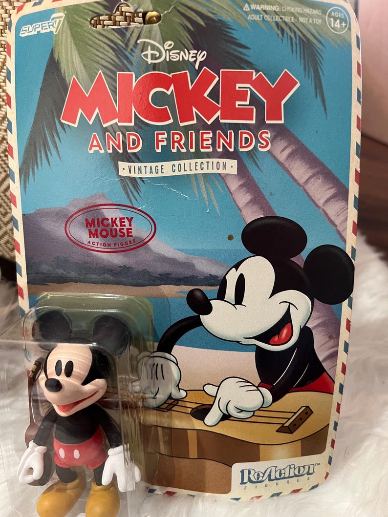 May include: Mickey Mouse and Friends Vintage Collection action figure. The packaging features Mickey Mouse playing a guitar, with a tropical background. The figure is in a clear plastic case. The packaging has the text "Mickey Mouse Action Figure".