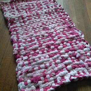 May include: A pink and white braided rug made from recycled fabric. The rug is woven in a checkered pattern.