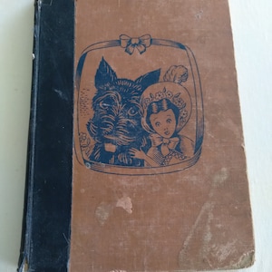 May include: A vintage book cover with a brown background and a black and white illustration of a dog and a girl wearing a hat. The illustration is framed with a black border and a bow at the top.
