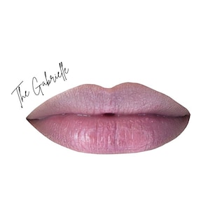 May include: A close-up of a pair of lips in a soft pink hue, with a subtle shimmer. The text "The Gabrielle" is written in a cursive font above the lips, set against a white background. The lips appear full and well-defined.