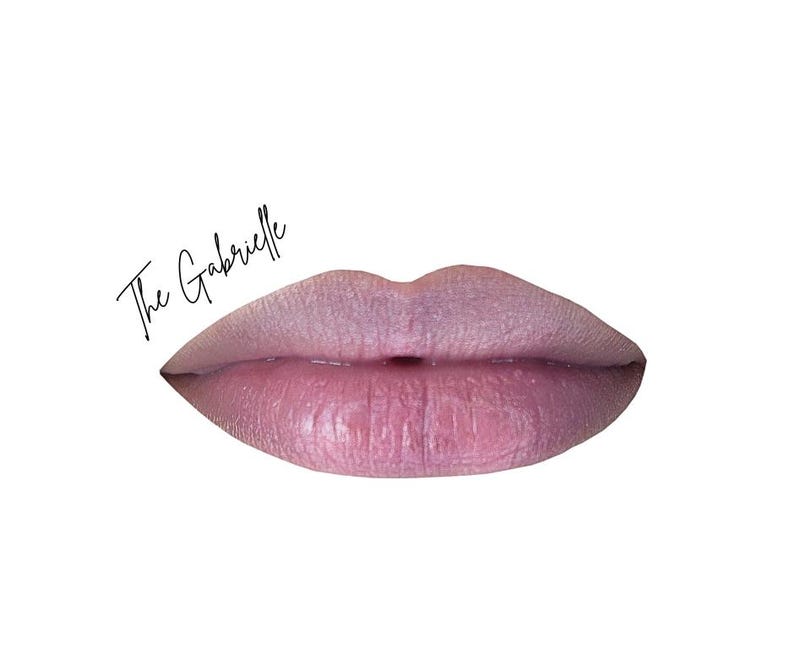 May include: A close-up of a pair of lips in a soft pink hue, with a subtle shimmer. The text "The Gabrielle" is written in a cursive font above the lips, set against a white background. The lips appear full and well-defined.
