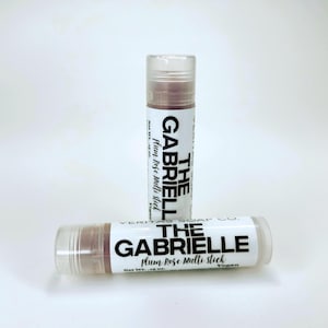 May include: Two lip balm tubes with clear caps and white labels. The labels read "THE GABRIELLE plum Rose multi stick" in black text. The lip balm inside is a reddish-brown colour. The tubes are on a white background.