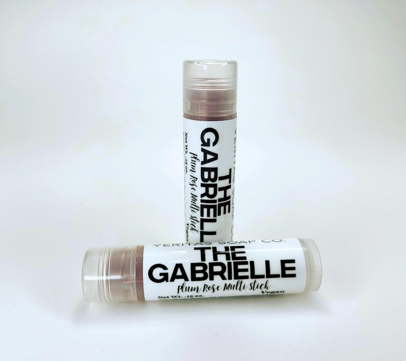 May include: Two lip balm tubes with clear caps and white labels. The labels read "THE GABRIELLE plum Rose multi stick" in black text. The lip balm inside is a reddish-brown colour. The tubes are on a white background.