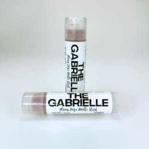 May include: Two lip balm tubes with the text "THE GABRIELLE Plum Rose Multi Stick" in black on a white background. The lip balm is a light plum colour. The tubes are clear with a white cap. Net weight is 4.25g.