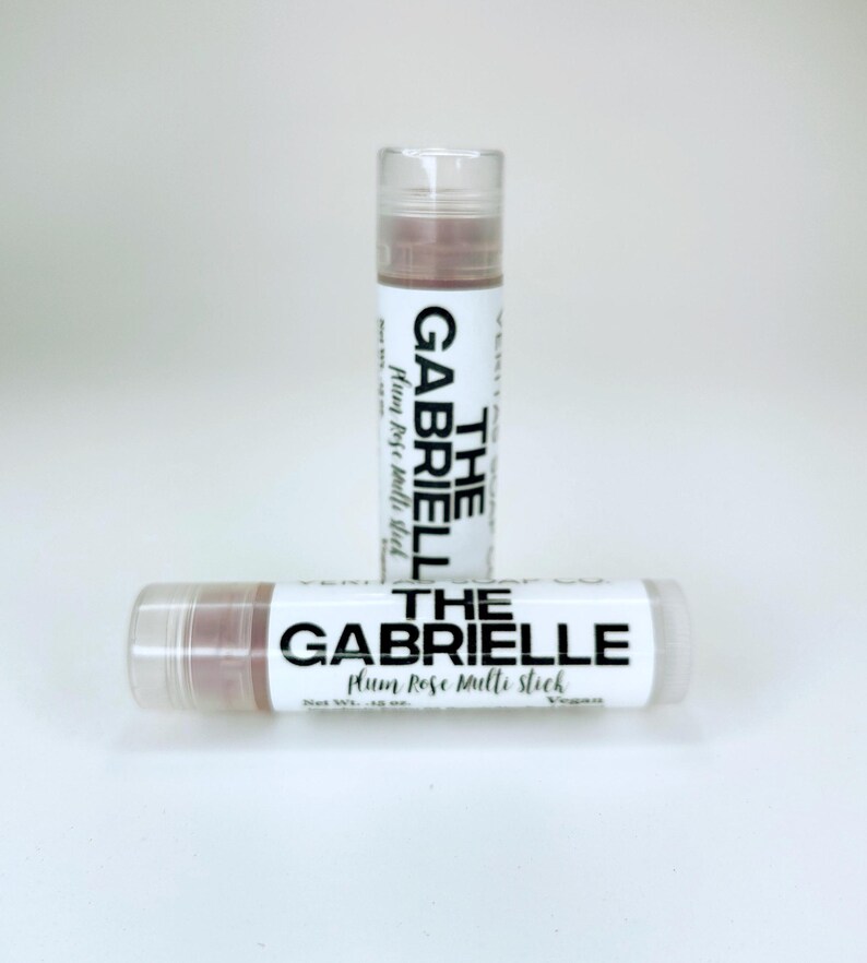May include: Two lip balm tubes with the text "THE GABRIELLE Plum Rose Multi Stick" in black on a white background. The lip balm is a light plum colour. The tubes are clear with a white cap. Net weight is 4.25g.