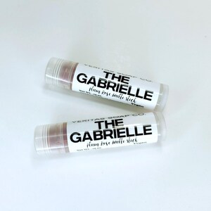 May include: Two lip balm tubes with clear caps and labels that read "THE GABRIELLE plum rose matte stick" in black text. The lip balm inside is a muted rose colour. The tubes are on a white surface.