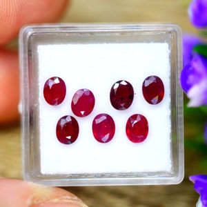 May include: Seven oval-shaped red gemstones in a white box. The gemstones are various shades of red.