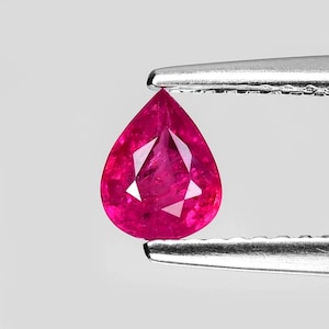 May include: A vibrant pink pear-shaped gemstone held in a pair of tweezers. The gemstone is faceted and has a high level of brilliance.