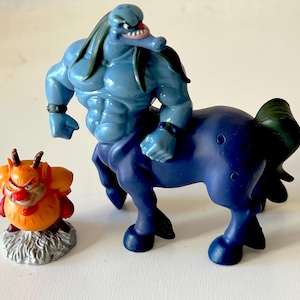 May include: A blue and purple centaur figurine with a green mane and a small orange and yellow creature figurine with horns.
