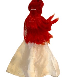 May include: A red haired doll wearing a white dress. The doll has long, flowing hair and is wearing a simple white dress.