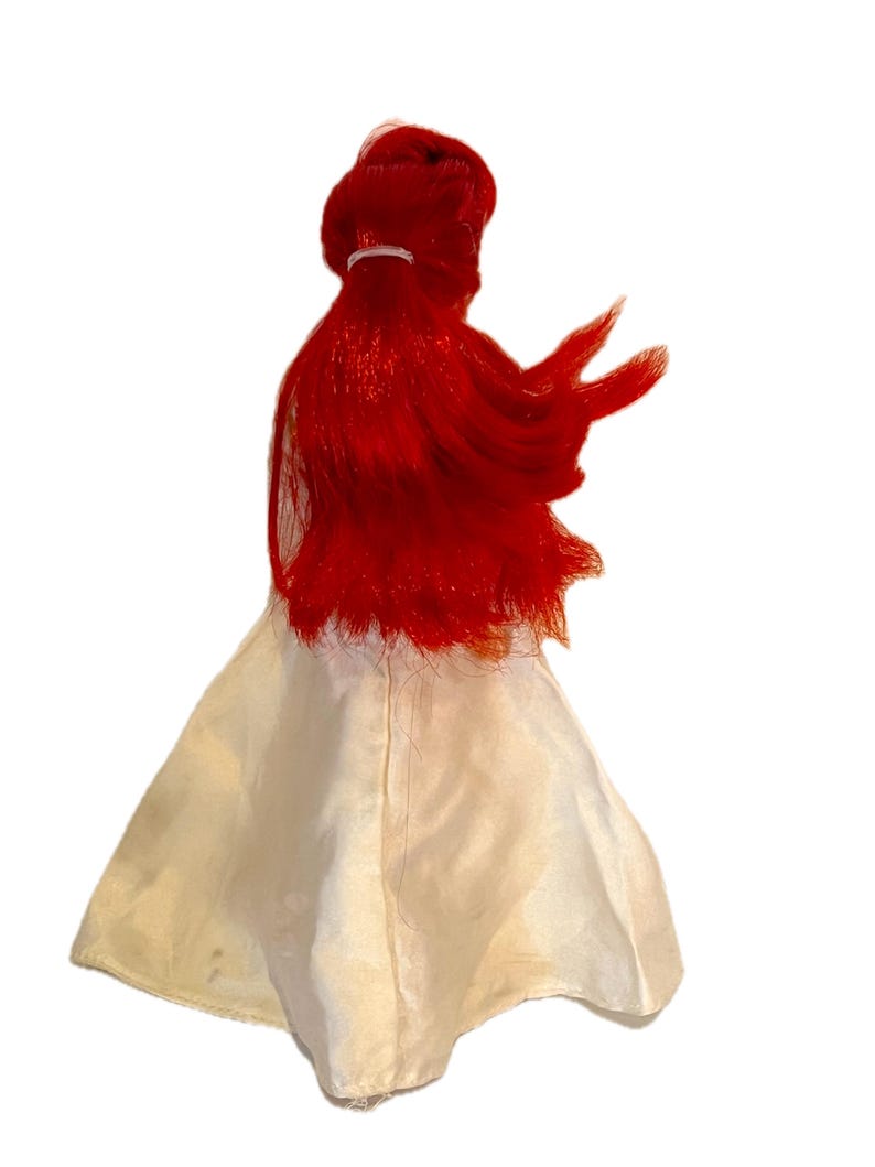 May include: A red haired doll wearing a white dress. The doll has long, flowing hair and is wearing a simple white dress.