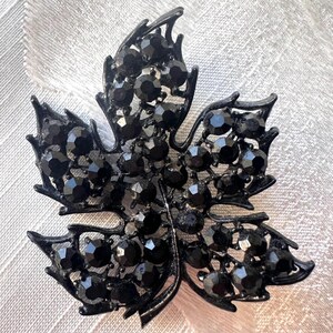 Puede incluir: Broche negro con forma de hoja, con un diseño detallado. La broche está cubierta de pequeñas piedras negras facetadas, lo que le da un aspecto brillante. La estructura metálica también es negra, creando un aspecto elegante. Adecuado para diversas ocasiones.