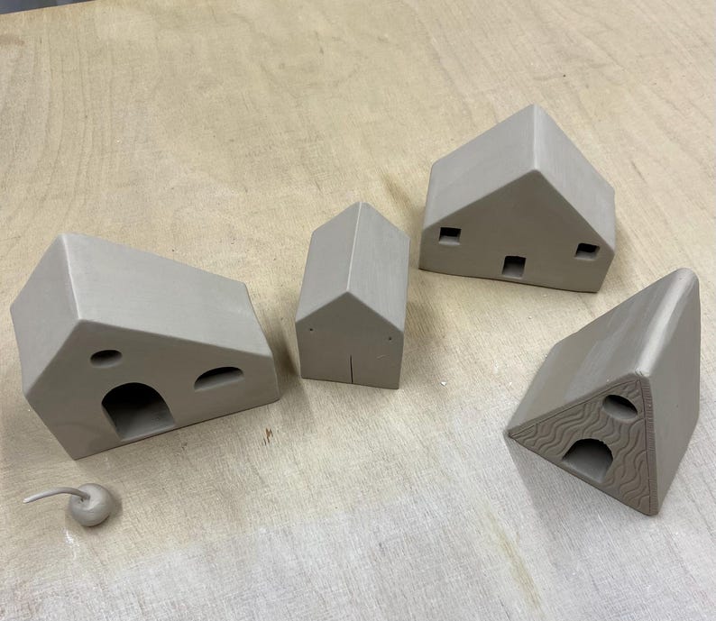 May include: Five small, unpainted, ceramic houses with different shapes and sizes. The houses have various openings and details.