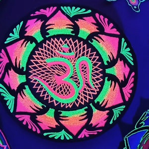 May include: Round, black embroidered patch with a neon pink and green Om symbol at the center, surrounded by a floral design. The patch glows under UV light. Other patches with similar designs are visible.