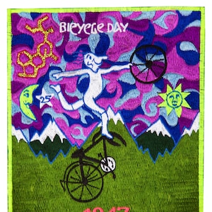 Puede incluir: Parche bordado con un diseño vibrante. El parche presenta una figura montando un monociclo en una montaña, con el texto "Bicycle Day" y el año "1943". El fondo incluye un sol, una luna y formas abstractas en tonos morados, azules y verdes.