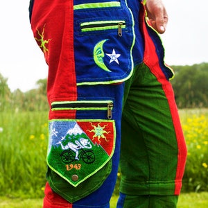 以下が含まれることがあります： 赤、青、緑のパネルを使用したカラフルなパッチワークパンツ。太陽、月、山のデザインが刺繍されたパッチとジッパー付きポケットが特徴です。ユニークで人目を引くデザインのパンツです。