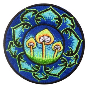 Puede incluir: Parche bordado con tres setas estilizadas con sombreros naranjas y branquias blancas, sobre un área de hierba verde. El diseño está enmarcado por un patrón floral azul con acentos negros y verde claro, todo sobre un fondo azul oscuro.