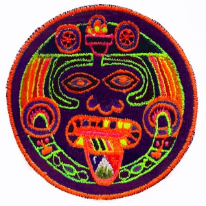 May include: A circular embroidered patch with a colorful design of a face with a large mouth and tongue. The face is surrounded by a circular border with geometric patterns. The colors are bright and vibrant, including orange, green, pink, and purple.