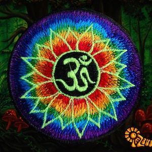 Pode incluir: Um remendo redondo bordado com um design de mandala arco-íris. O centro da mandala apresenta um círculo preto com um símbolo Om verde.