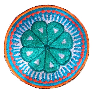 Puede incluir: Un parche redondo bordado con un diseño azul, blanco y naranja. El centro del parche presenta una flor verde de cinco puntas.