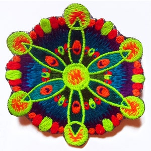 Könnte beinhalten: Ein lebendiger, gestickter Aufnäher mit einem symmetrischen floralen Design. Das Kunstwerk zeigt einen zentralen neongrünen Kreis mit strahlenförmigen Blütenblättern in Türkis, Lila und Orange. Die Ränder sind in Neongrün und Rot umrandet, was einen auffälligen Kontrast erzeugt.