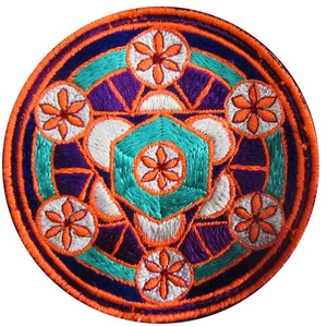 May include: A circular embroidered patch with a geometric design in shades of orange, teal, white, and purple. The center of the patch features a teal hexagonal shape with a white flower in the center.
