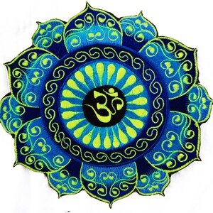 May include: Embroidered patch featuring a lotus flower design in shades of blue and green. The center displays the Om symbol in black. The patch has a detailed, ornate pattern, suitable for clothing or accessories.
