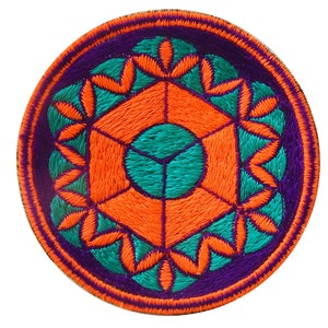 May include: Circular embroidered patch with a geometric design. The patch features a vibrant color scheme of orange, teal, and purple. The design includes a central hexagon surrounded by floral-like shapes, all set against a purple background.