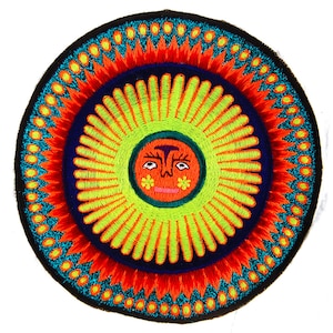 Könnte beinhalten: Ein runder gestickter Patch mit einer leuchtend gelben Sonne mit einem lächelnden Gesicht in der Mitte. Die Sonne ist von konzentrischen Kreisen in Rot, Blau und Grün umgeben.