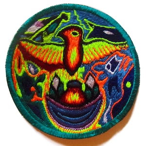 Puede incluir: Parche redondo bordado con un diseño vibrante. Presenta un motivo central de ave en naranja, rojo y amarillo, sobre un fondo azul, verde y morado. El parche tiene un borde turquesa, creando una obra de arte detallada y colorida.