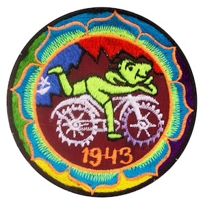 Puede incluir: Un parche bordado colorido con una figura verde montando una bicicleta con engranajes. El parche tiene un diseño de mandala de colores arcoíris alrededor del borde y el año "1943" en el centro.