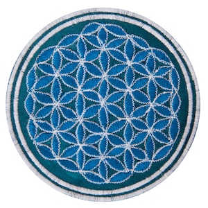 Op de afbeelding: Ronde geborduurde patch met een blauw en wit bloemenpatroon. Het heeft een teal groene rand met witte en teal stiksels. Het centrale ontwerp is een gedetailleerd patroon van onderling verbonden blauwe vormen.