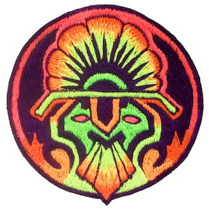 Peut inclure: Un patch brodé circulaire avec un motif coloré. Le motif représente un visage stylisé avec une couronne et une barbe. Les couleurs sont vives et vibrantes, notamment le vert, l'orange, le jaune et le violet.