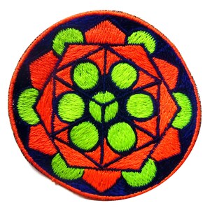May include: Round embroidered patch with a geometric design. The patch features a vibrant color scheme of orange, green, and blue. The design includes a central flower-like shape surrounded by geometric patterns. The patch is likely for clothing or accessories.