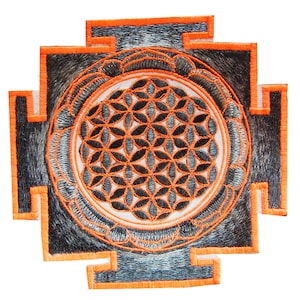 Peut inclure: Écusson brodé avec un motif géométrique, présentant un motif central de fleur de vie. Le patch a une forme carrée avec une bordure orange et un fond gris et noir. La fleur de vie est noire et orange.