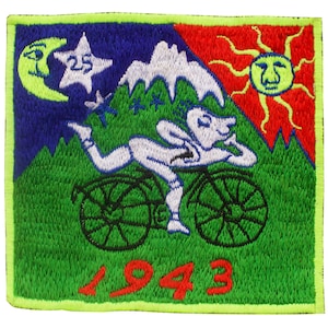 Peut inclure: Un patch brodé vert, rouge, bleu et blanc avec un personnage de dessin animé à vélo. Le personnage est blanc avec une tête bleue et roule sur un vélo noir à deux roues. Le patch a une bordure jaune et l'année 1943 est brodée en rouge en bas.