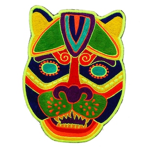 Puede incluir: Parche bordado con un rostro de jaguar estilizado. El diseño incorpora colores vibrantes como verde, amarillo, naranja, rojo, morado y azul. El parche tiene una apariencia detallada y texturizada, con un estilo gráfico audaz.
