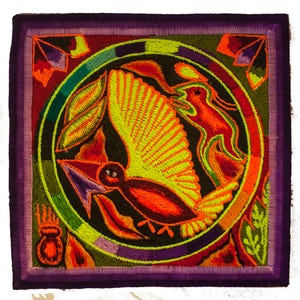 Pode incluir: Têxtil bordado quadrado com um desenho circular central representando um pássaro em voo, rodeado por folhas e outras figuras estilizadas. A paleta de cores inclui tons vibrantes de laranja, amarelo, verde e roxo, sobre um fundo preto.