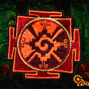 Pode incluir: Patch bordado com um design geométrico em tons de vermelho, laranja e castanho, com uma borda verde. O patch tem uma borda preta e está sobre um fundo de floresta. O logotipo "Zauberwald" está no canto inferior direito.