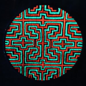 Pode incluir: Remendo bordado circular com um design geométrico em laranja néon e verde-azulado. O design apresenta um padrão repetitivo de linhas e formas interligadas sobre um fundo preto. O remendo é provavelmente para roupas ou acessórios.