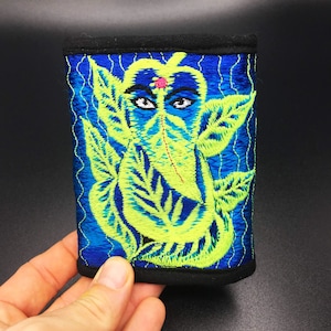May include: Embroidered rectangular patch featuring a vibrant depiction of a deity with a blue background and neon green accents. The design includes detailed facial features and leaf-like patterns, with a black border.